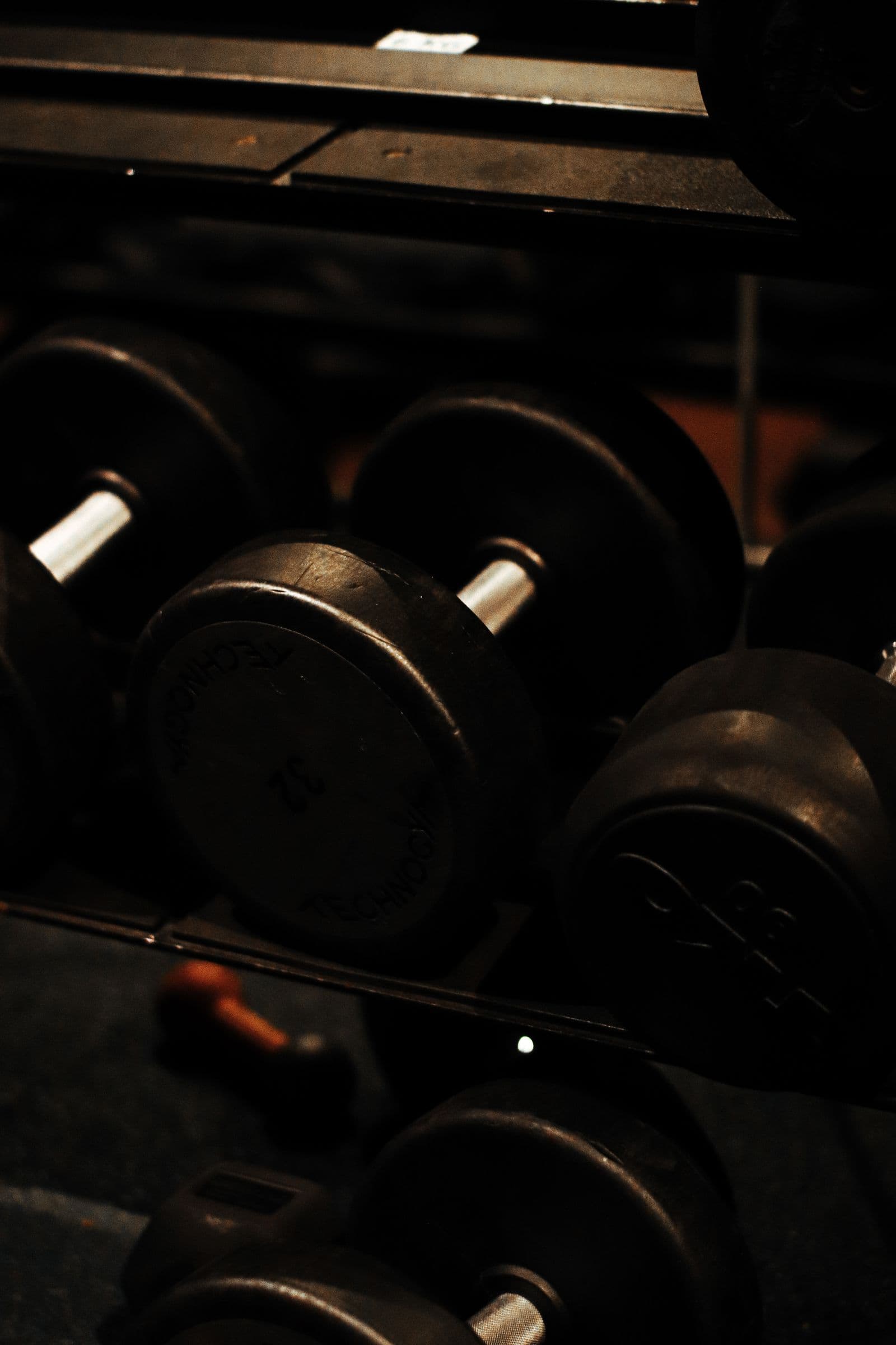 A rack of heavy dumbbells lined up in a dark gym